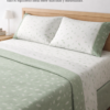Sábana encimera blanca con estampado verde del juego de cama Lys de Pierre Cardin Paris, extendida sobre la cama con vivo verde y embozo a juego, mostrando un diseño elegante y atemporal.