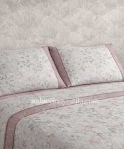 Juego de sábanas Pierre Cardin Paris Jade con bajera rosa lisa, sábana encimera blanca estampada con flores y almohadas a juego con embozo lateral rosa y vivo decorativo, presentado sobre cama con papel pintado neutro.