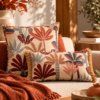 Conjunto de cojines Antilo Brezo en color caldera con estampado botánico en tonos terracota, beige y azul grisáceo, cojín cuadrado sin flecos y rectangular con flecos decorativos.
